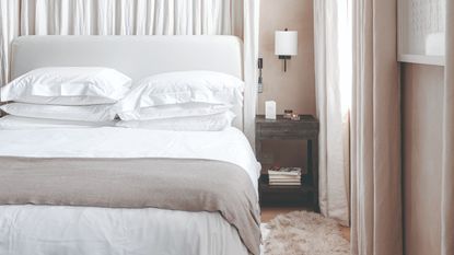 White bedroom with elongated grey headboard, modern wall lights and woven ceiling light