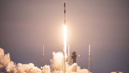 a white and black rocket launches into a dusk sky, leaving behind a puffy plume