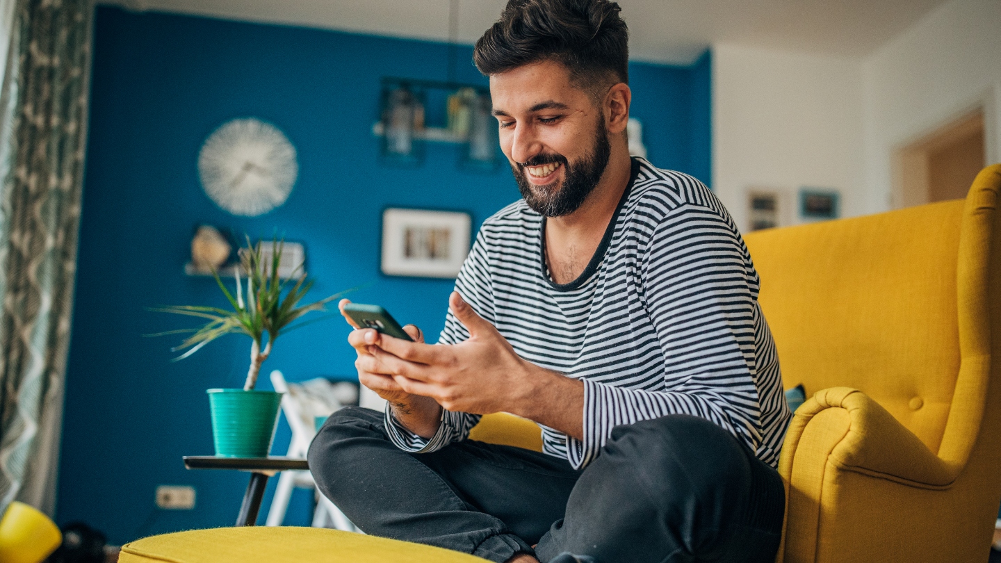 Man sitting on yellow arm chair smiling at his phone