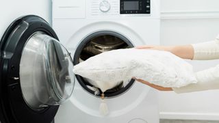 A woman's hand holding a pillow before she places it in a washing machine