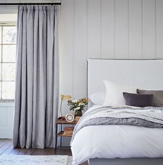 White bedroom with wall panelling, grey curtains and wooden flooring