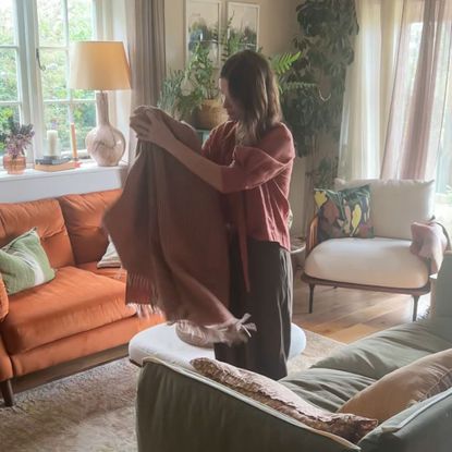 Woman in standing between sofas in living room folding up throw
