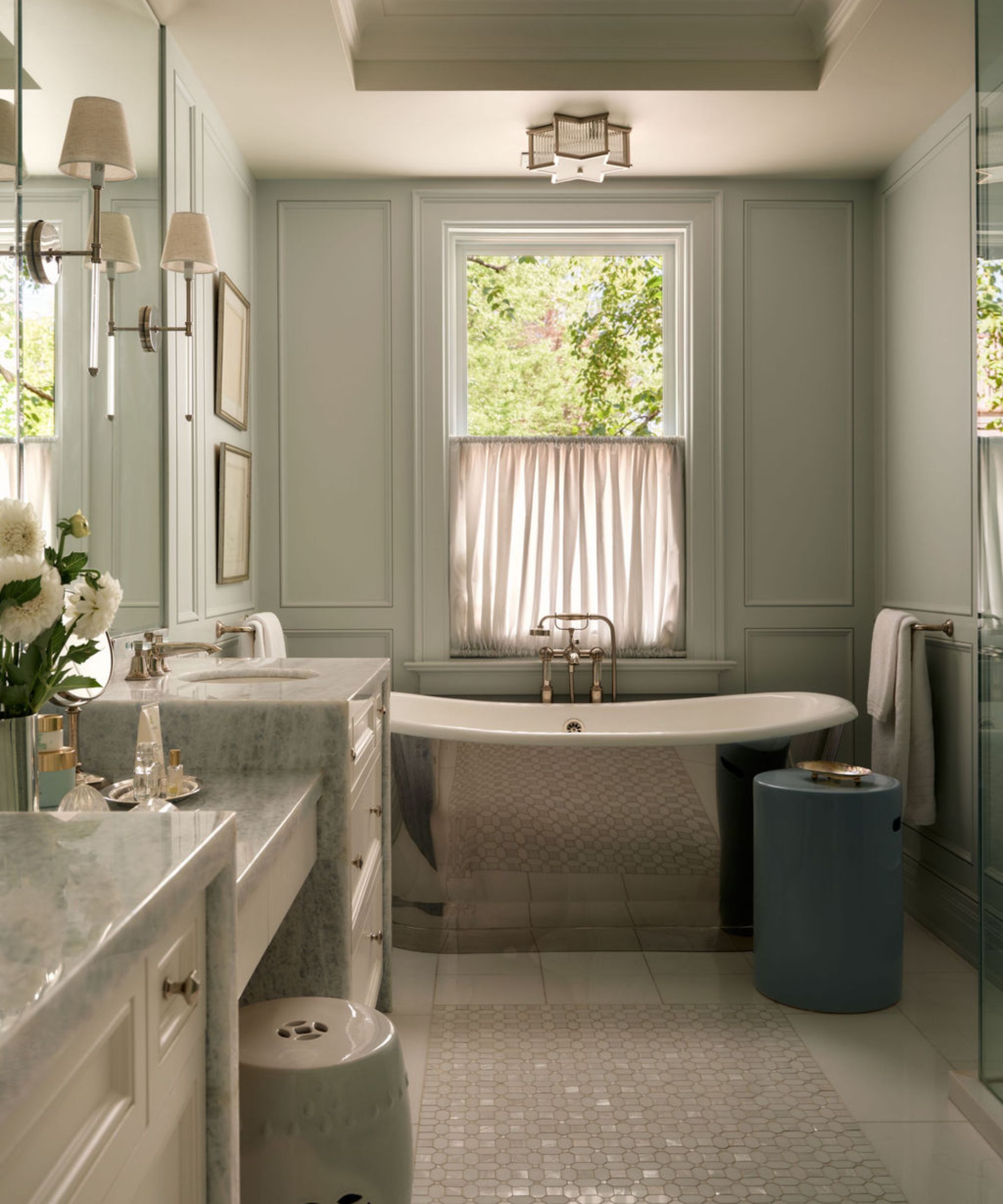 a layered light blue gray ensuite bathroom with a silver freestanding tub and marble vanity