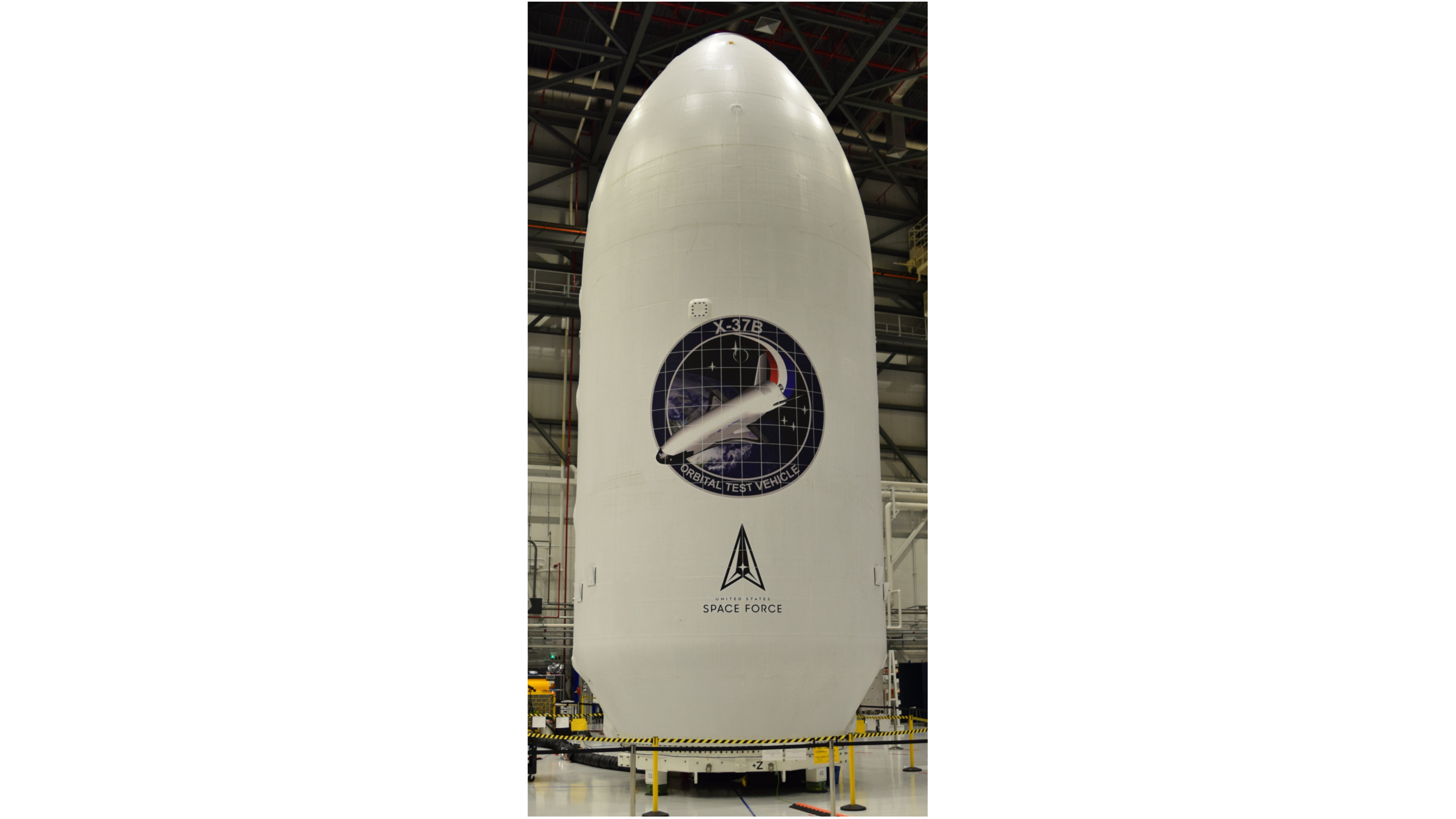 a large, conical white payload fairing sits inside a hangar.