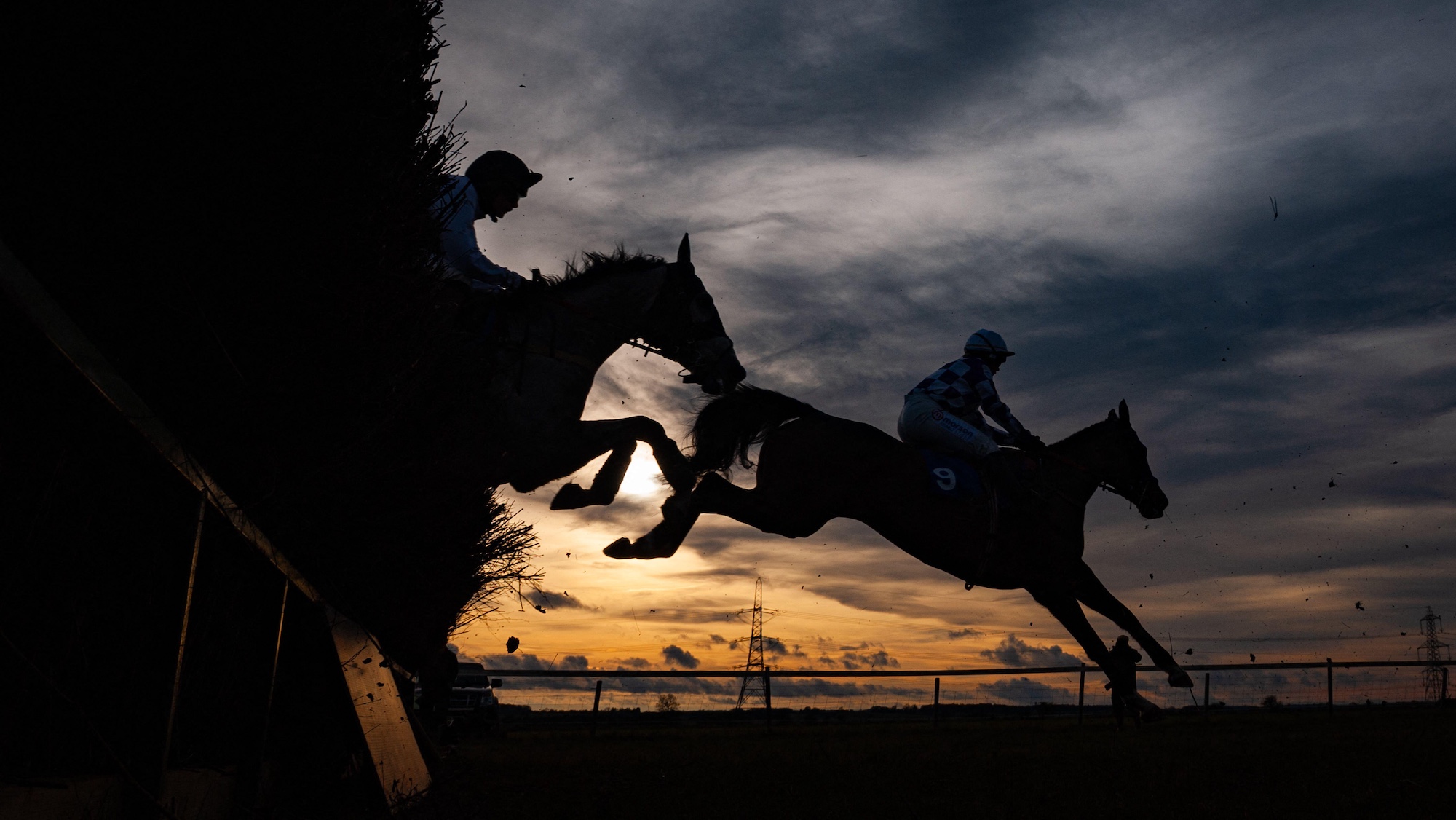 Image shows a silhouette of two racehorses jumping over a fence at a point-to-point.