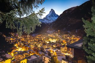 Buildings in Zermatt are illuminated at night below the snow-covered Matterhorn