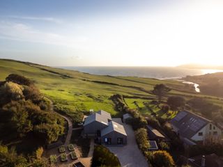 An overhead image of a barn conversion on a cliffside looking out to the coast beyond