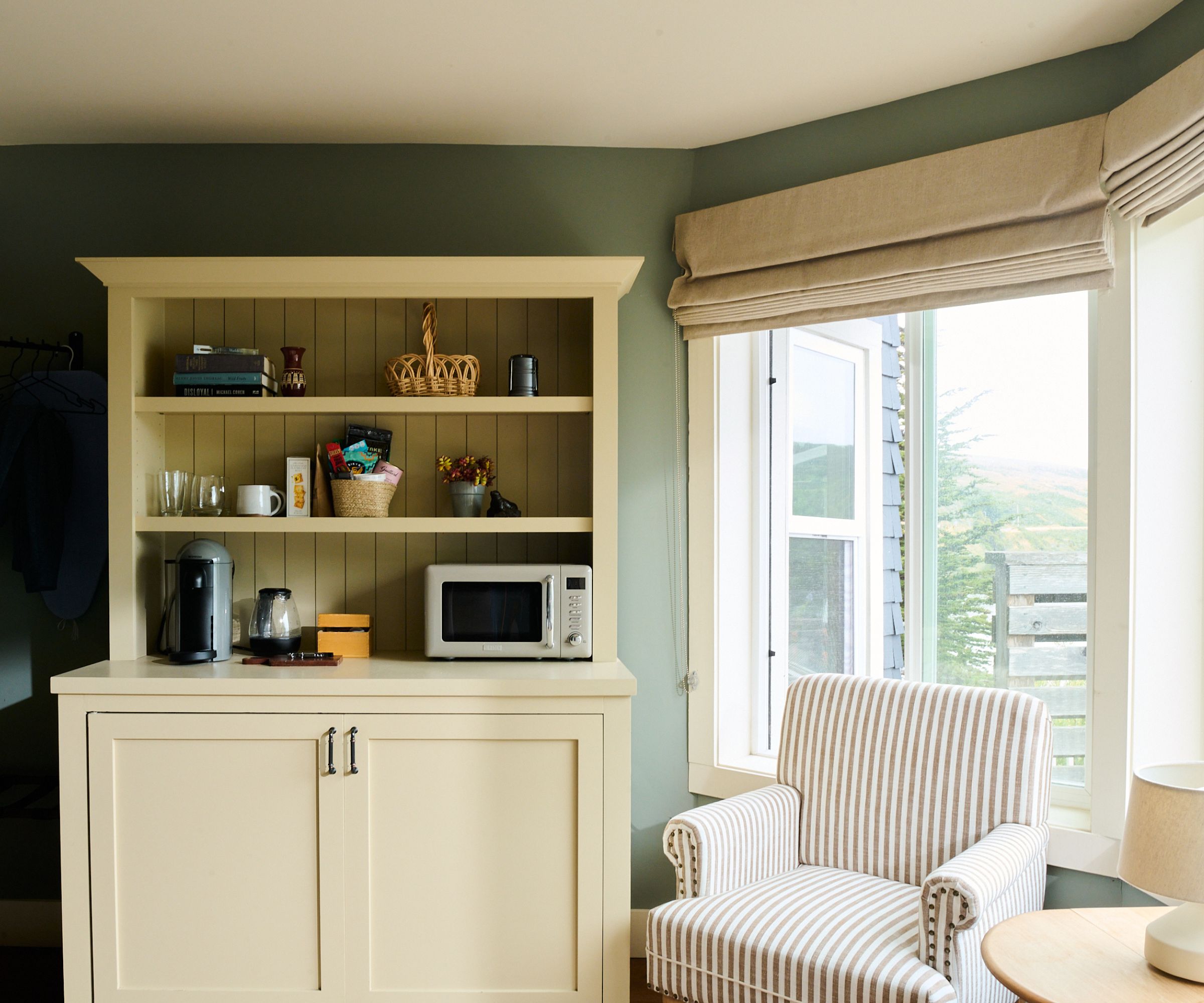 living room with green walls, beige cabinet and striped armchair in front of a window