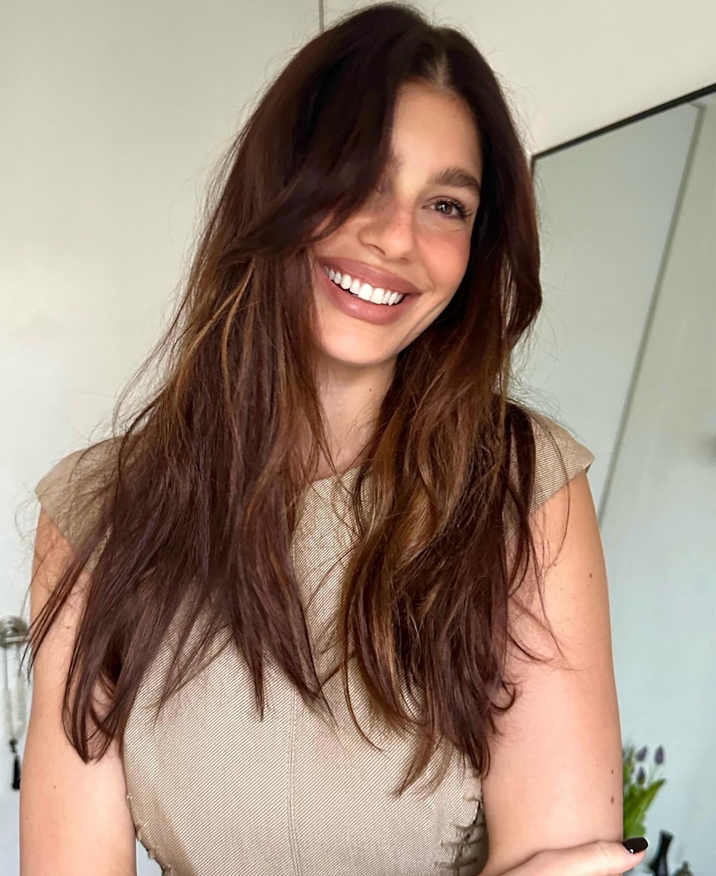 Camila Morrone souriant à la caméra avec des cheveux bruns usés
