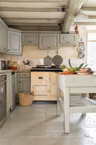 a period kitchen with a white aga and gray kitchen units, with a white butchers block i the middle sat on the gray tiled floor