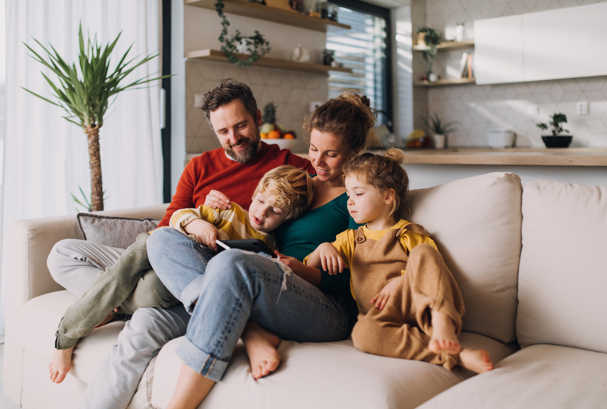 A family of 4, a father, a mother, a son and a daughter all sat on a couch together looking at a tablet