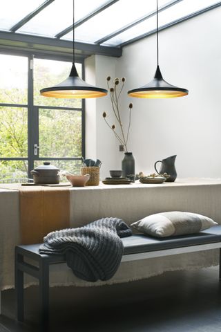 modern rustic dining room with linen and bench, two black pendant lights and black tableware, black floor