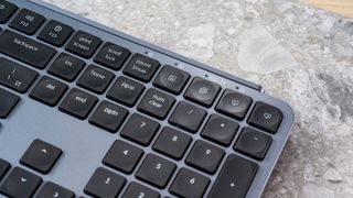 a black and grey budget wireless Bluetooth keyboard with a full-size layout and a numerical keypad is photographed against a blue background