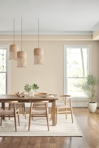 A dining room with soft beige walls, a wooden mid-century style dining table, and three pendant lights