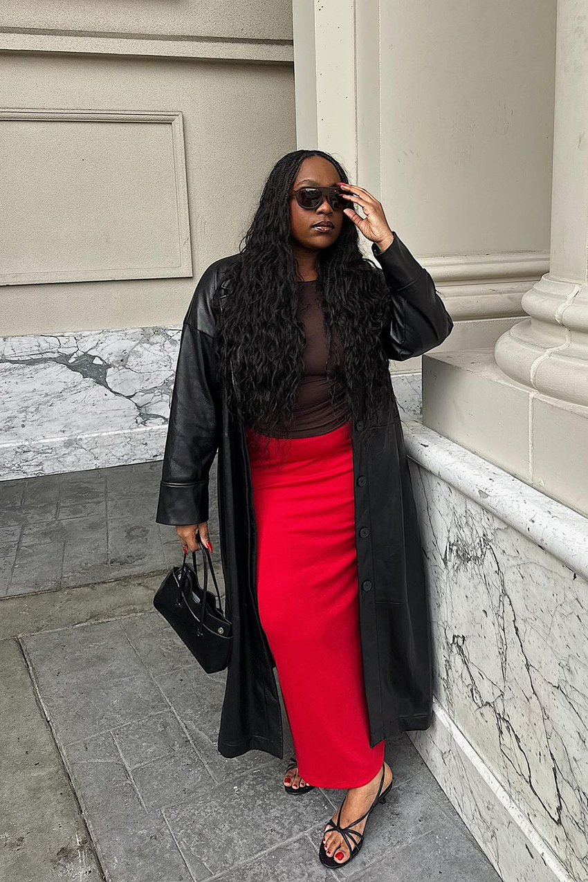 A woman wearing a black leather coat, red skirt, and sheer top