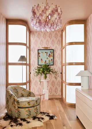 A closet space in a b bedroom with a white dresser, pink patterned wallpaper, and a floral upholstered barrel chair