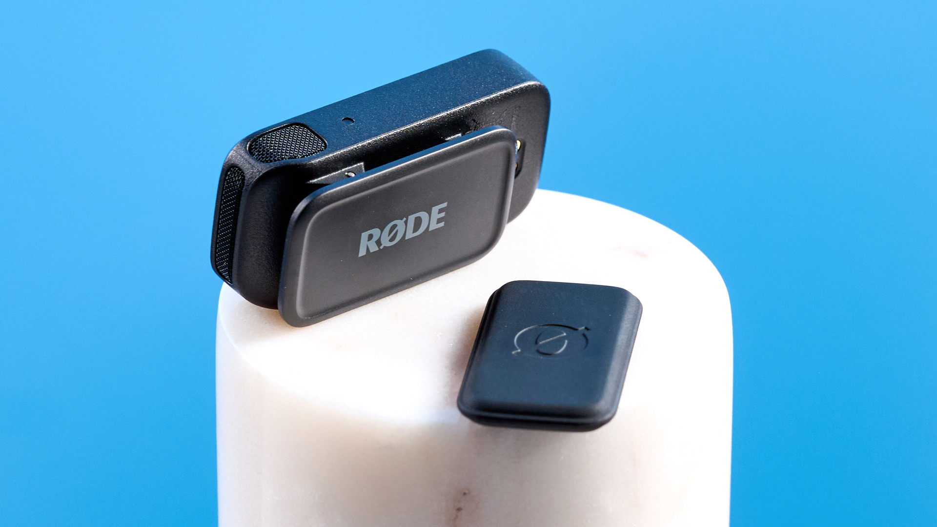 the rode wireless micro microphone with the black charging case and two black transmitter mics photographed against a blue background