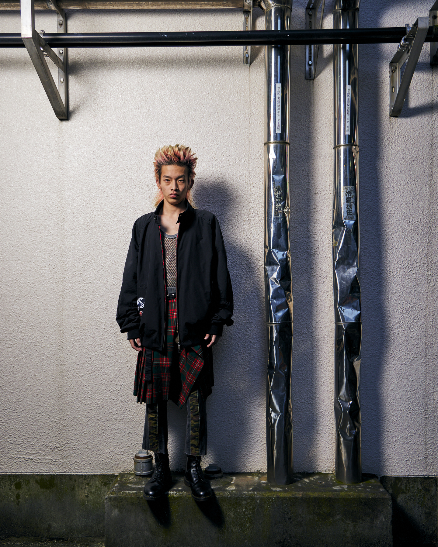 Man in Baracuta x Junya Watanabe jacket on white industrial wall