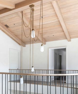 Landing with light wooden paneled ceiling, white painted walls, black stair railings, hanging bulb pendants on wire