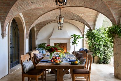 Outdoor table under vaulted ceiling with pale stone flooring and pizza oven 