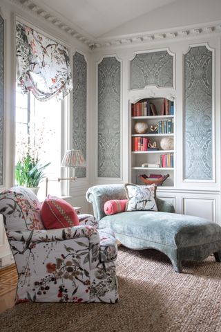 white living room with grey damask wallpaper panels, blue chaise, floral armchair, matching blind, coir rug