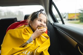 Beautiful child eating a doughnut while looking through a car window
