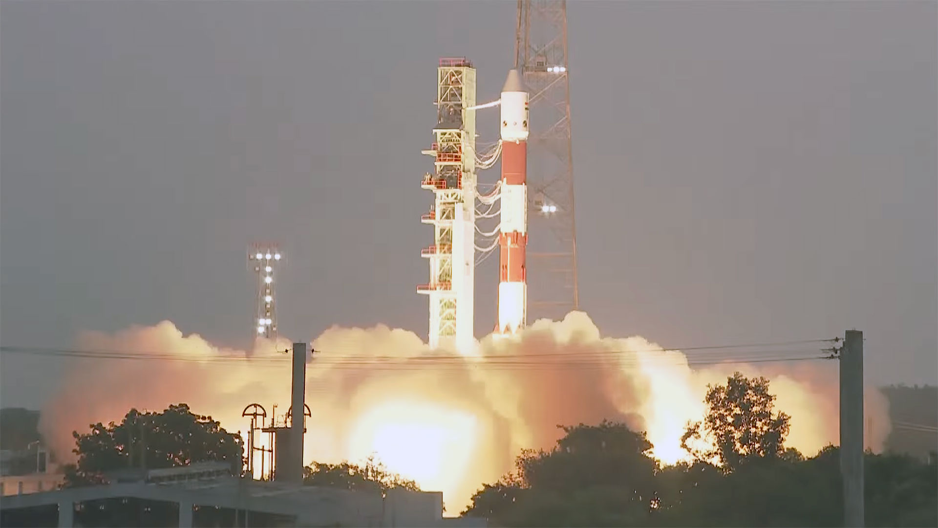 an orange and white striped rocket lifts off into the dawn sky.
