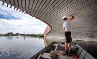 A man standing in a boat, inspects the underside of the bridge