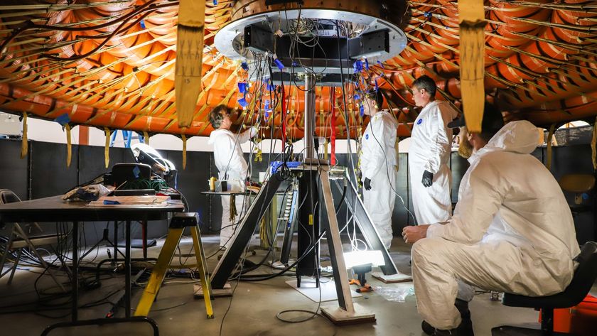scientists in clean suits stand beneath a large inflatable round structure bound with multiple straps