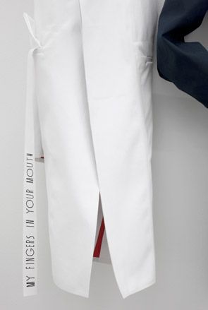 Close up view of a white coat by Carlo Brandelli featuring a strip that says 'My Fingers In Your Mouth' at Matthew Brannon's show