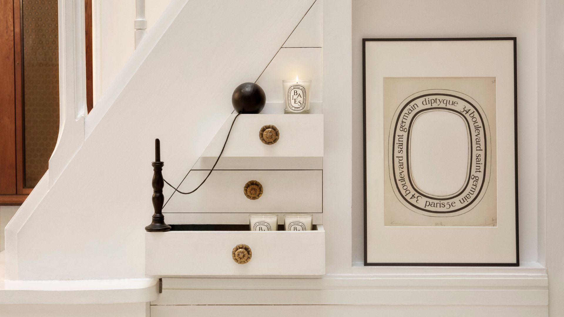 A set of drawers by a staircase with Diptyque candles