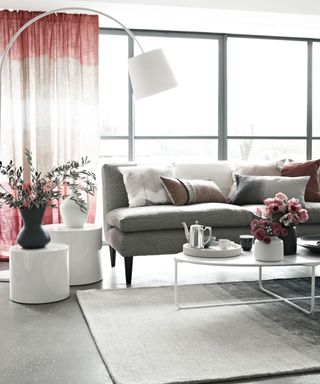 grey floor living room with colorful curtains and a grey sofa with dye-like cushions and a white coffee table with flowers and a tea-pot