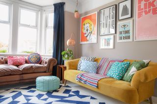 Plaster pink living room with yellow velvet sofa, brown leather sofa, blue and white geometric rug and bright gallery wall