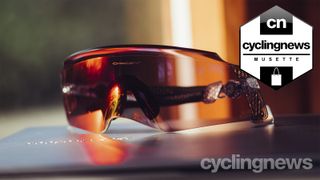 A pair of red tinted sunglasses rests atop a laptop in the sunshine by a window