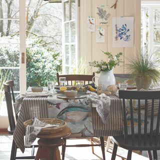 A set dining table with a thin striped tablecloth in white and blue and fish-print table runners