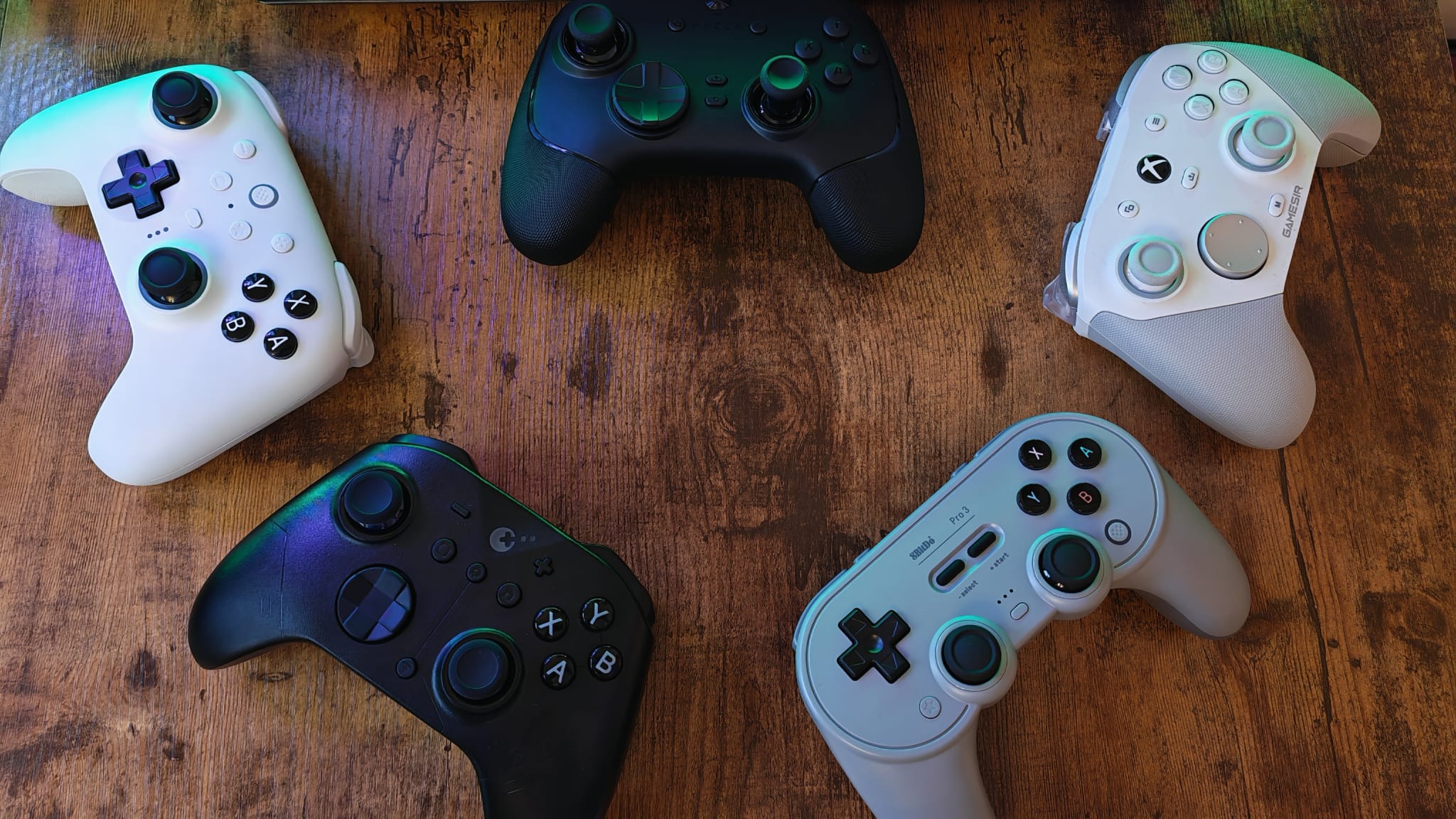 Five different gaming controllers for PC scattered around a desktop surface