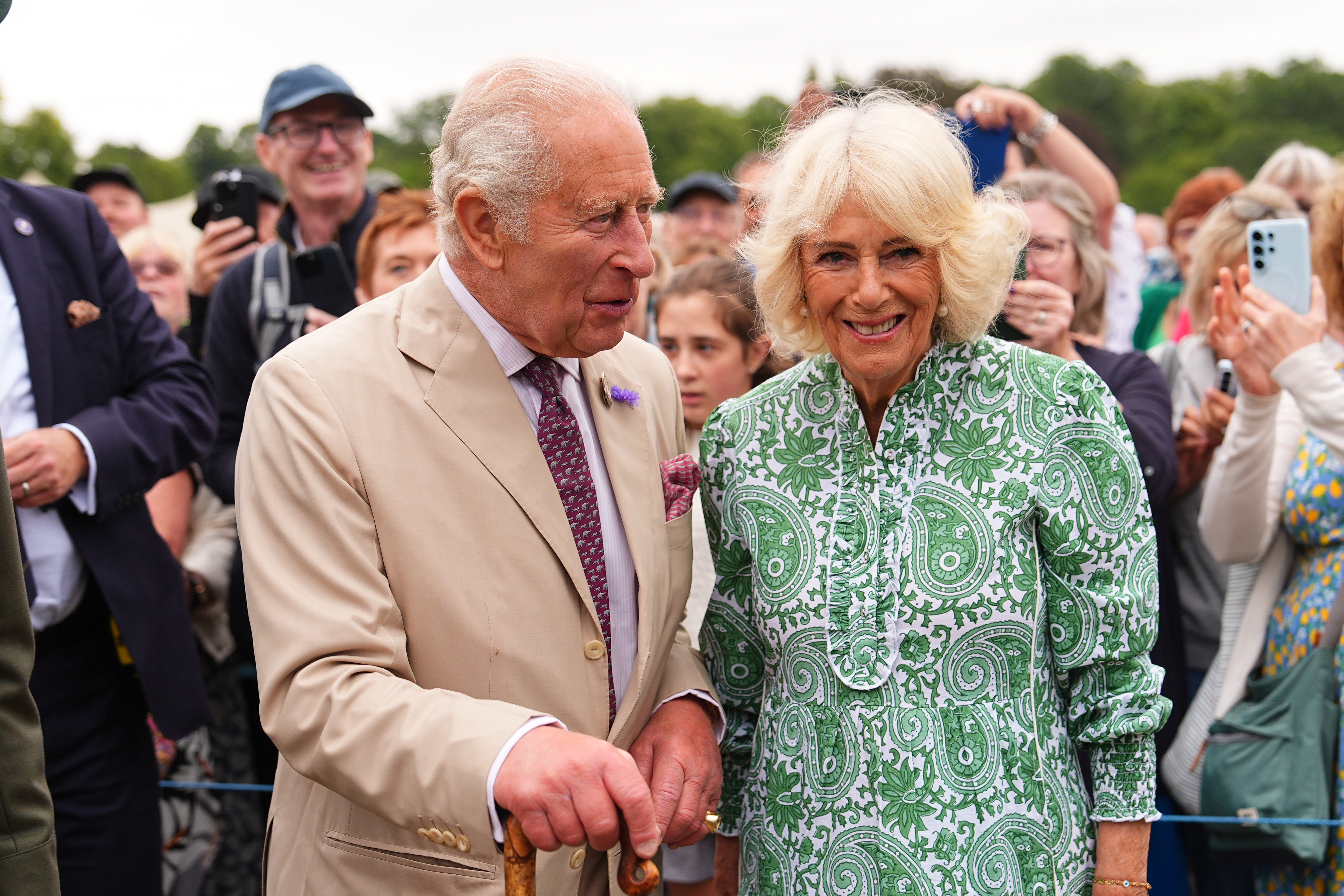 Queen Camilla and King Charles smiling in front of a group of fans at the Sandringham Flower Show