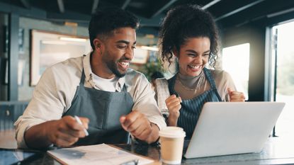 Two business owners celebrate as they look at a laptop together.