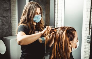 Hairdresser wearing a mask braiding a woman's hair