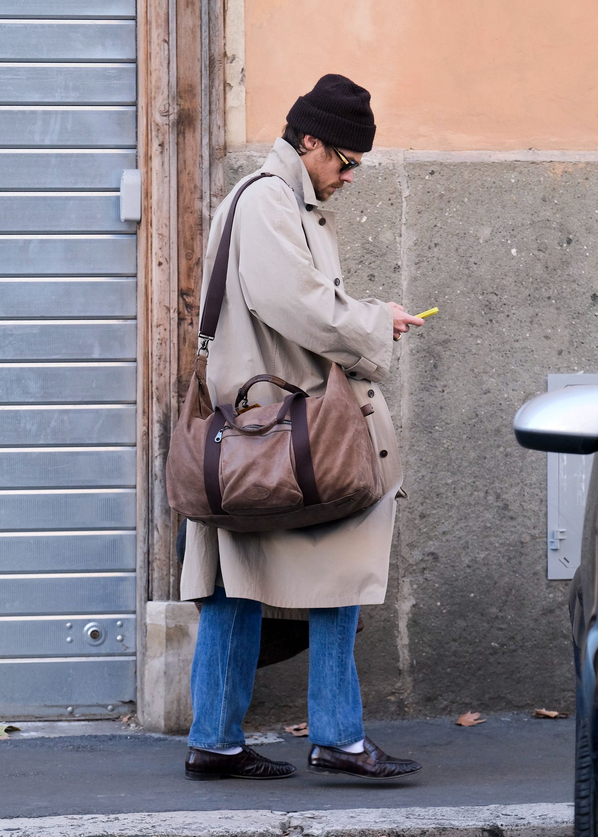 Harry styles wears eel-leather loafers with jeans and a trench coat.