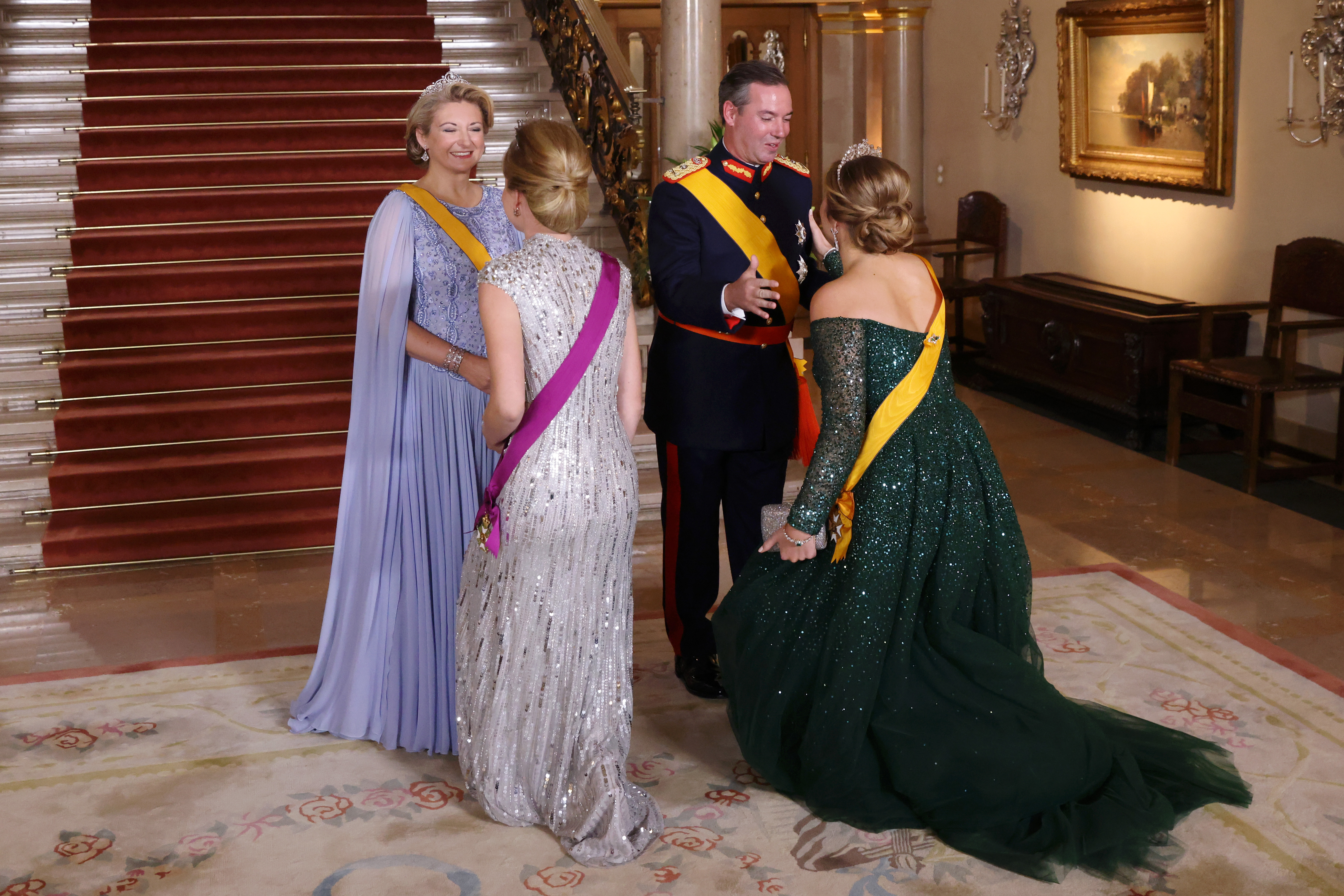 Princess Elisabeth curtsying to Grand Duchess Stephanie, and Princess Catharina-Amalia curtsying to Grand Duke Guillaume, wearing evening gowns and military uniform in front of a staircase