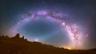 glowing arch of milky way above a desert landscape with stars