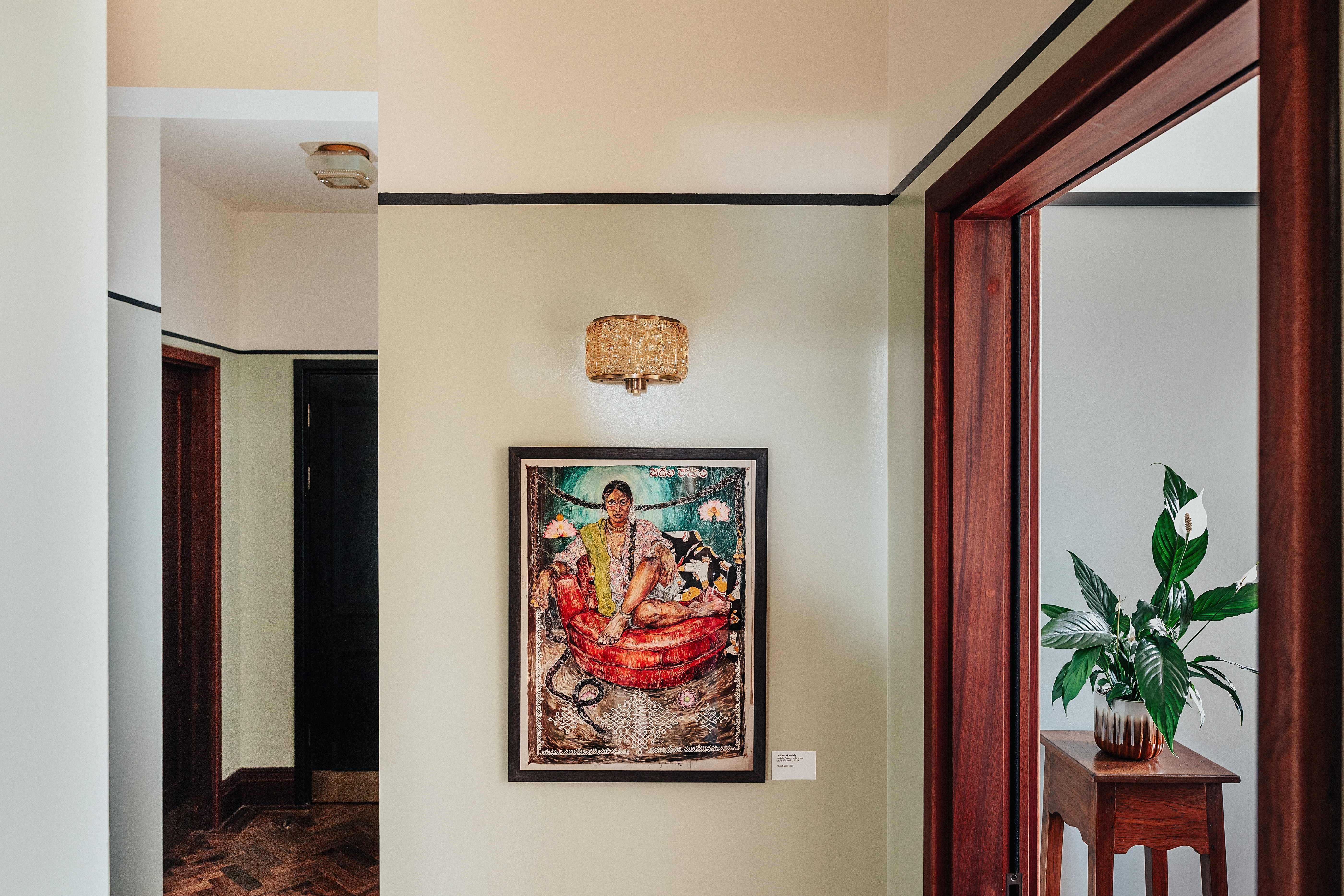 A layered, transitional hotel suite featuring a series of figurative, colorful artworks on its walls, patterned furniture, including rugs, armchairs, and sofas, split-color pillars, and a buttery, tile blue, and green palette.