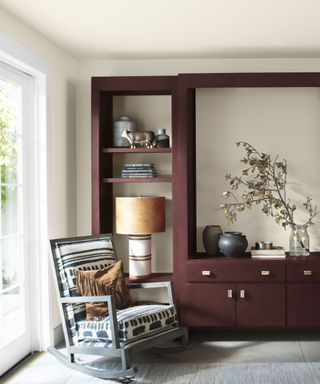 Living room with cream painted walls and burgundy painted cabinetry, lounge chair and table lamp