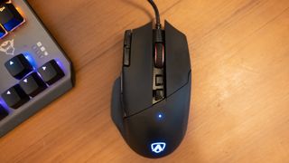 A black AOC AGM600 gaming mouse sitting on a brown wooden desk