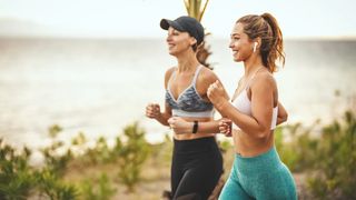 Two women power walking outdoors by the ocean smiling