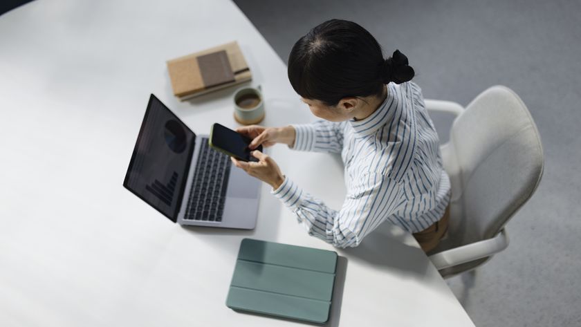 High angle view of businesswoman text messaging on smart phone while working on a computer in the office.