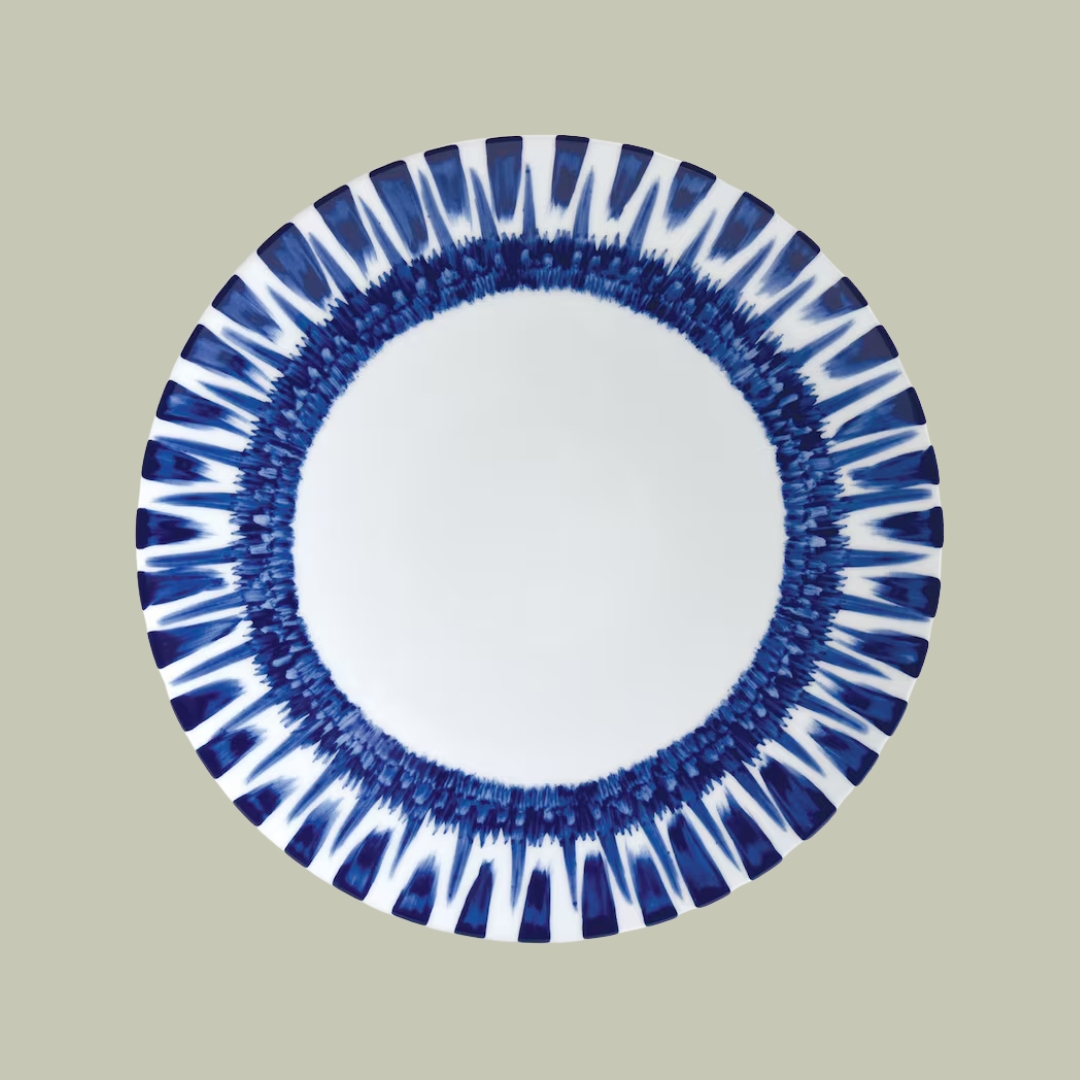 A porcelain, white and blue plate with a sun rays-like rim decoration sits against a pale green background.