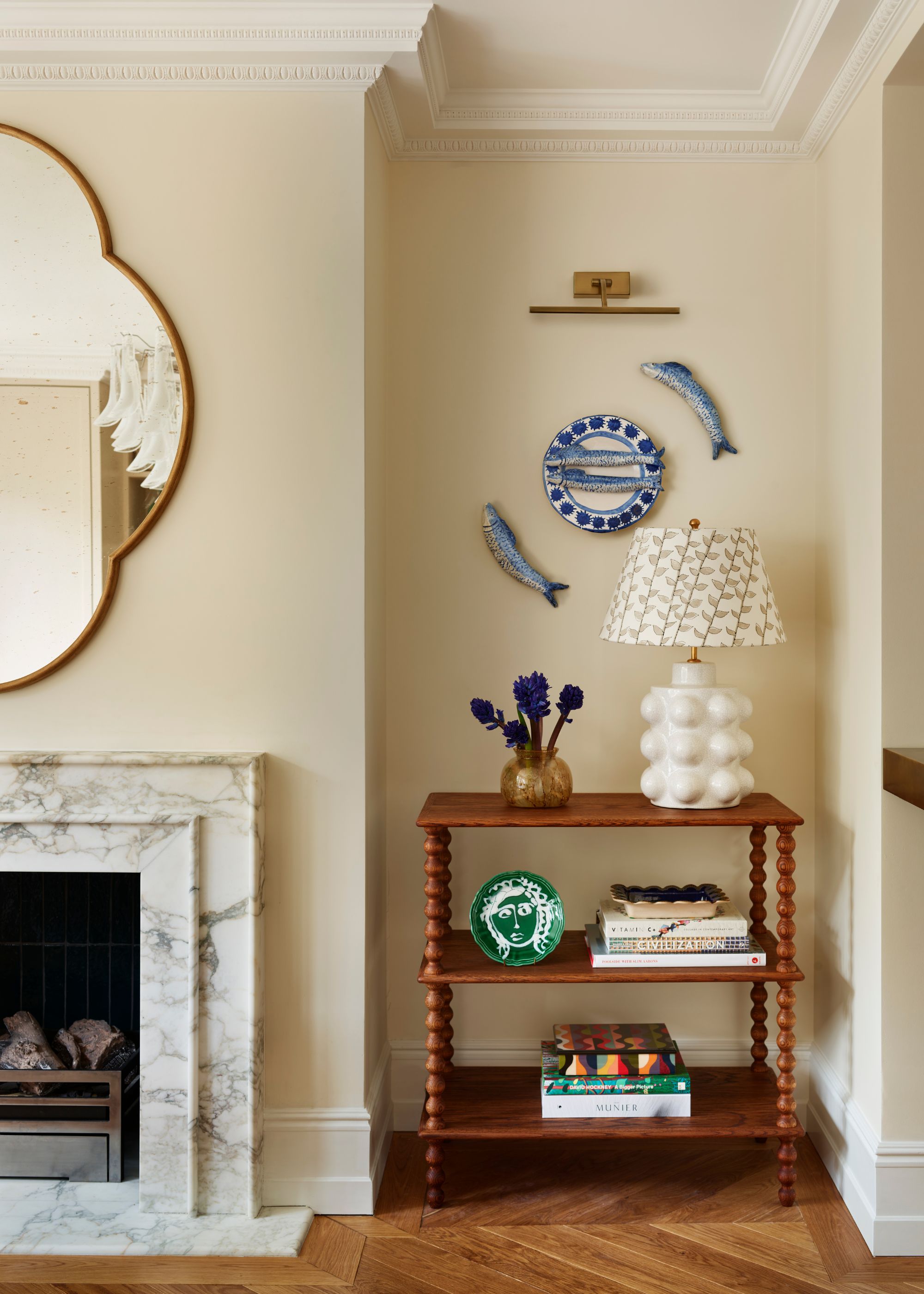 A dining room with warm white walls, parquet flooring, a marble fireplace, and a wooden dresser in an alcove with decorative objects.