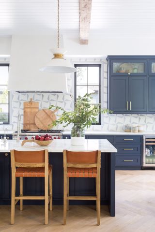 A kitchen with blue units and a kitchen island with a white marble counter top and wooden dining stools